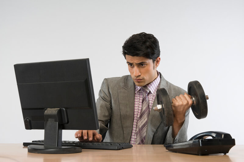 Businessman exercising with dumbbells and working on a computer