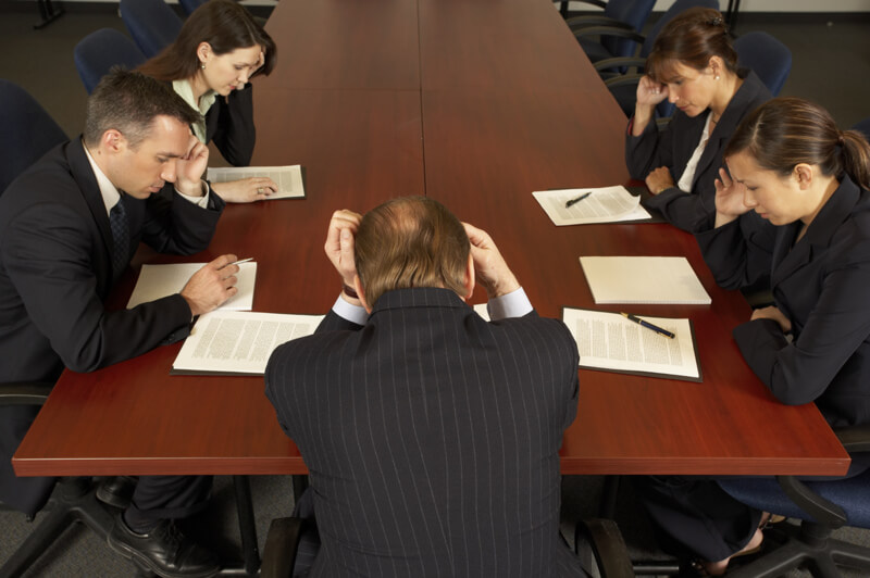 group of businesspeople sitting at conference table appearing upset